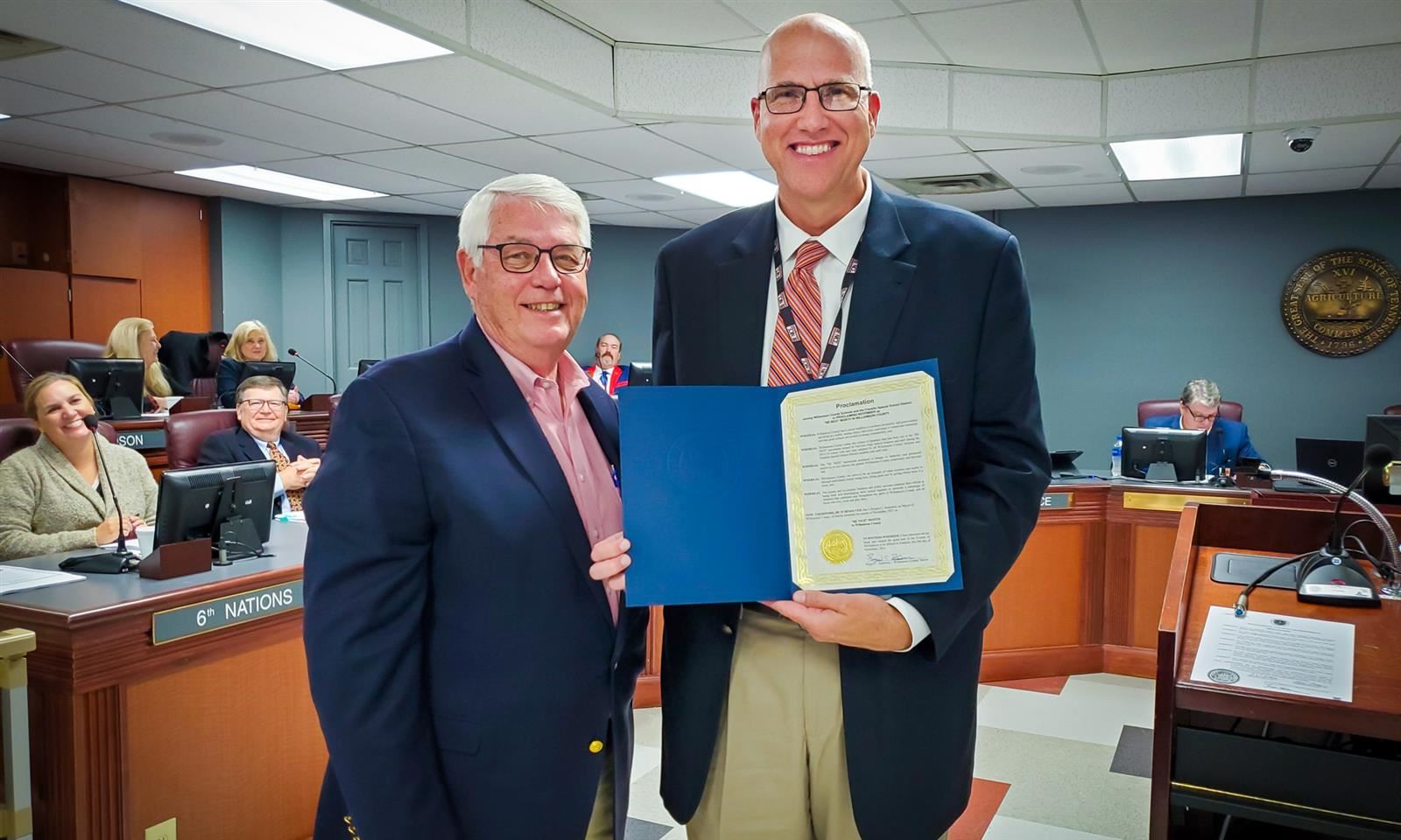 Two men hold up a certificate proclaiming BE NICE Month in Williamson County